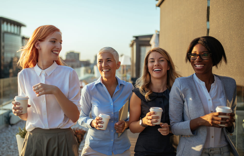 Four business women walking together with coffee cups and smiling